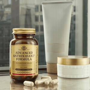 Solgar Advanced Antioxidant Formula vegetable capsules in a glass bottle against a window background on a table
