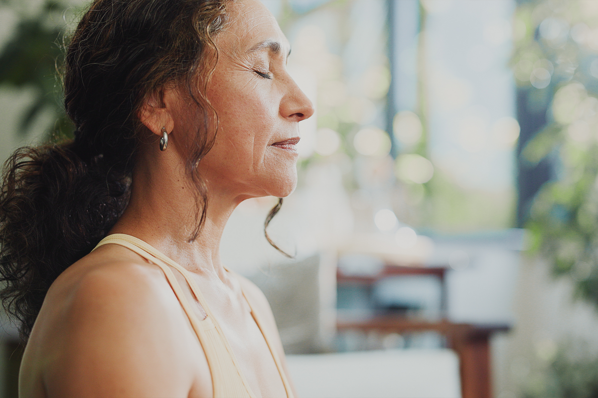 A woman with her eyes closed against a softly blurred indoor background with bright natural light.