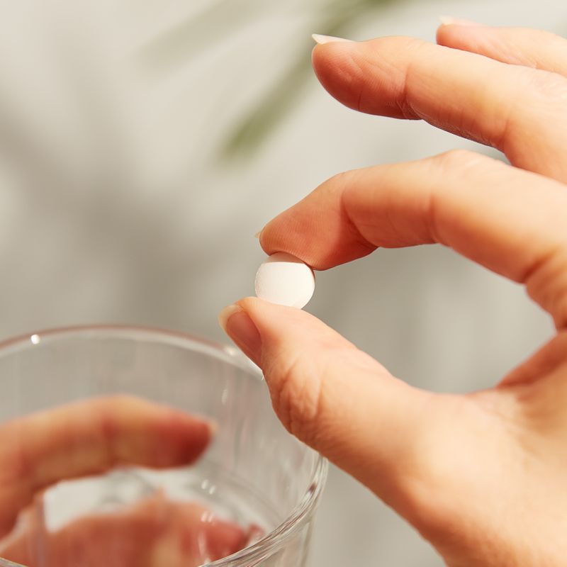 Solgar Chelated Zinc Tablet in a person's hand with a glass of water