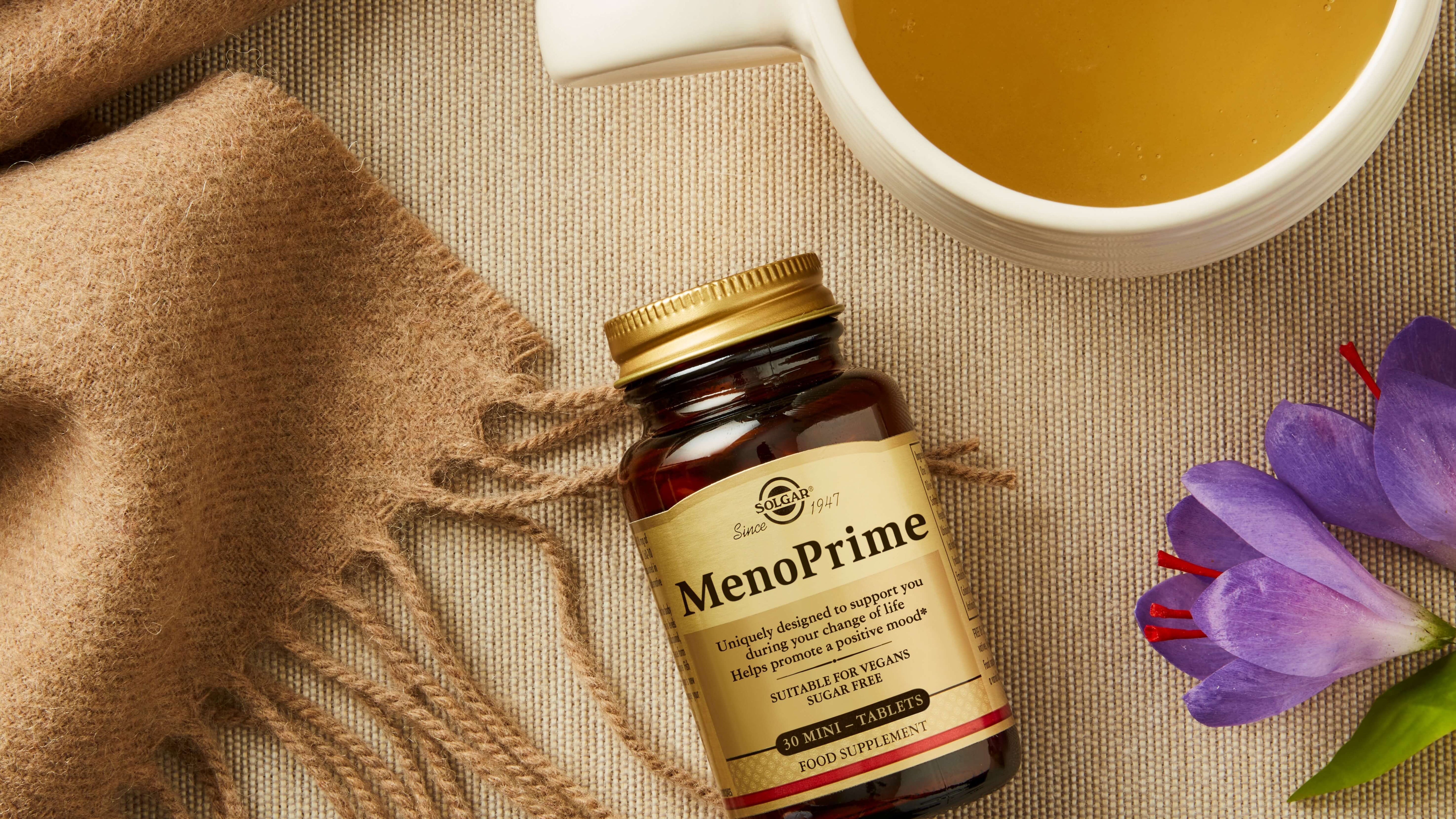 Solgar MenoPrime vitamins next to green tea and purple flowers a table