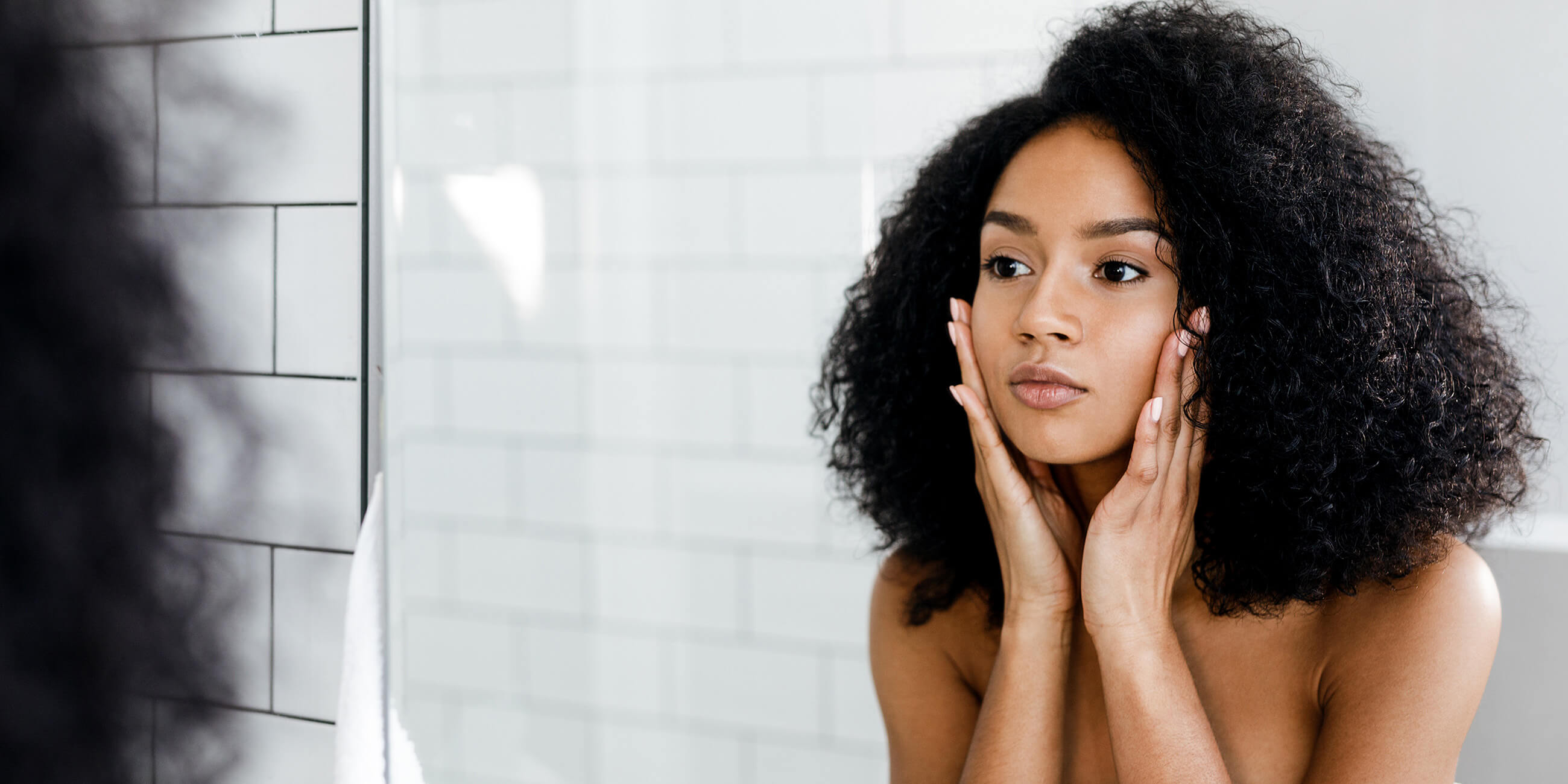 A woman looking in the mirror at her healthy skin as a result of Solgar protein powder