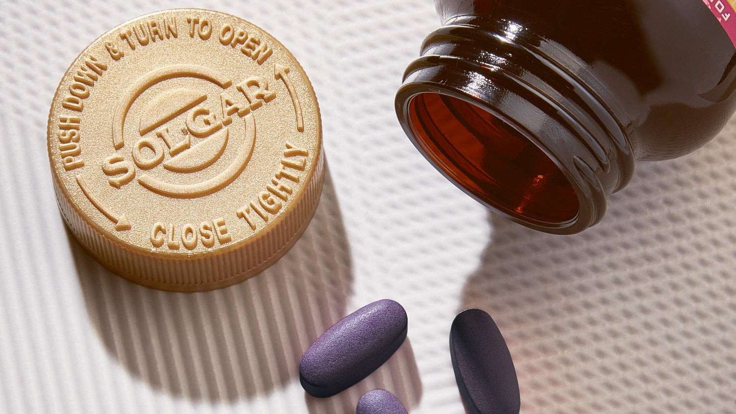 Open Solgar Multivitamins bottle with child-proof cap beside 3 purple tablets on a textured surface.