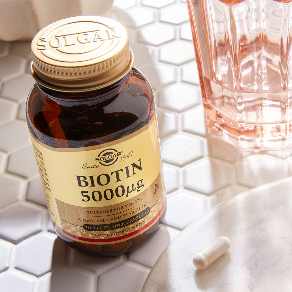 Solgar Biotin Vitamins on a table next to a glass of water