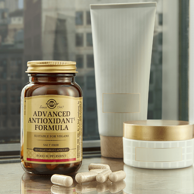 Solgar Advanced Antioxidant Formula vegetable capsules in a glass bottle against a window background on a table