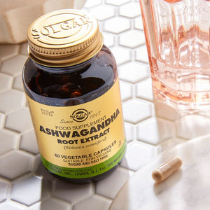Solgar Ashwagandha Root Extract Vegetable Capsules in a glass jar on a table with some water