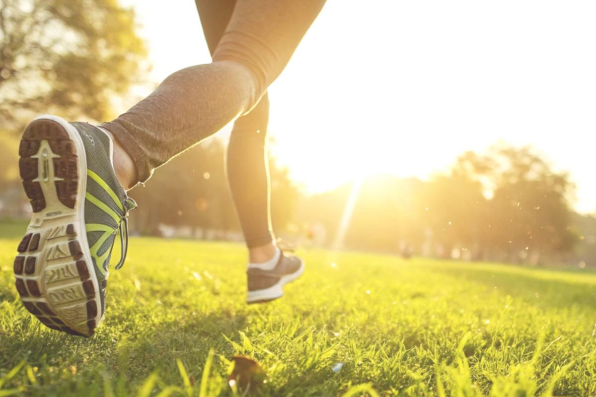 A close-up action shot of a person's legs running through a grassy park with the sun shining