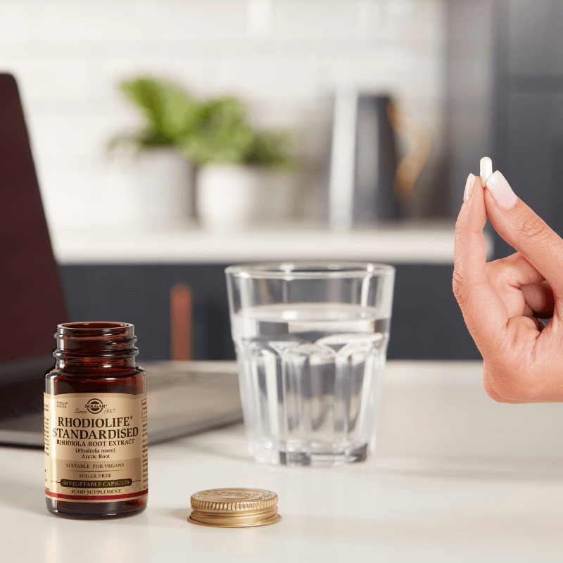 Solgar Rhodiola Root Extract vegetable capsules in a glass bottle on a table next to some water
