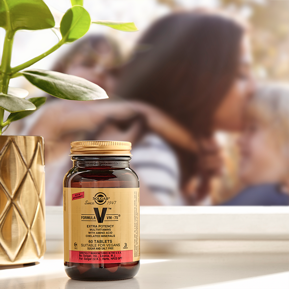 Solgar Formula VM-75 dietary supplement bottle on a surface with a blurred background of people and a plant.