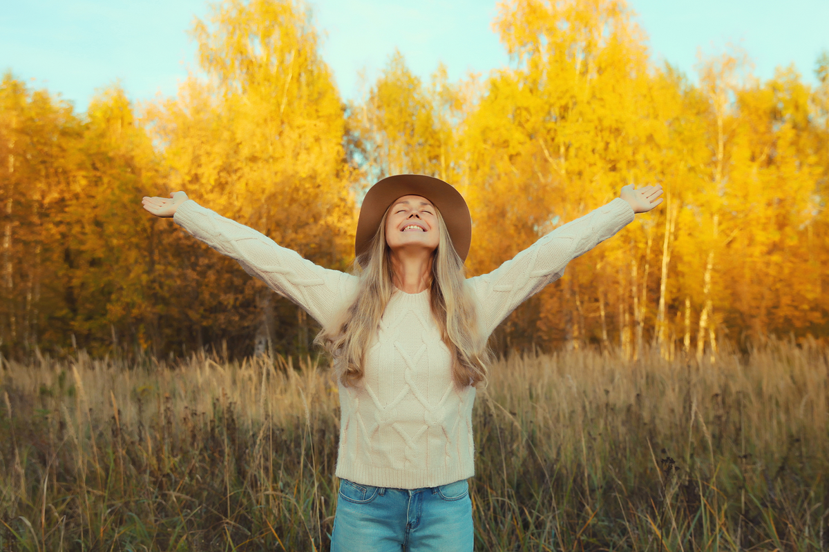 Woman in an autumnal field smiling with her arms spread out