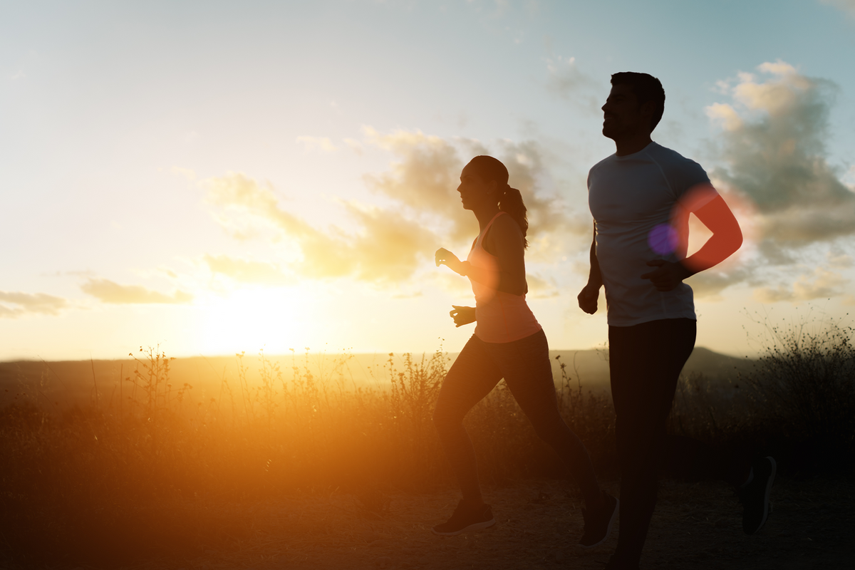 Man and woman jogging outdoors in a grassy field together with the sun shining. 